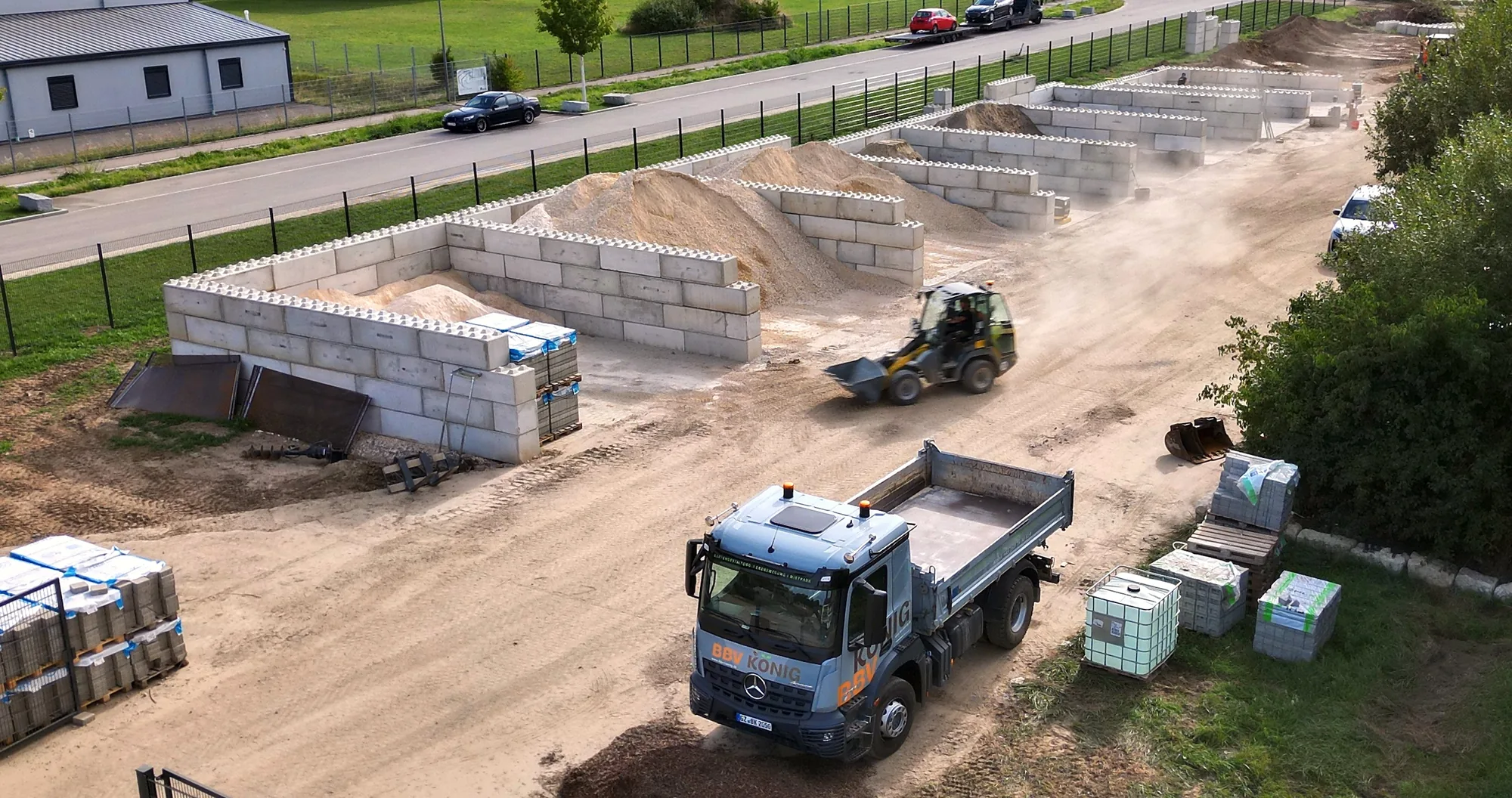 Luftaufnahme des Lagerplatzes von BBV König in Leipheim: Boxen aus Betonblöcken mit Sand und Kies, Radlader und eigener Kipper