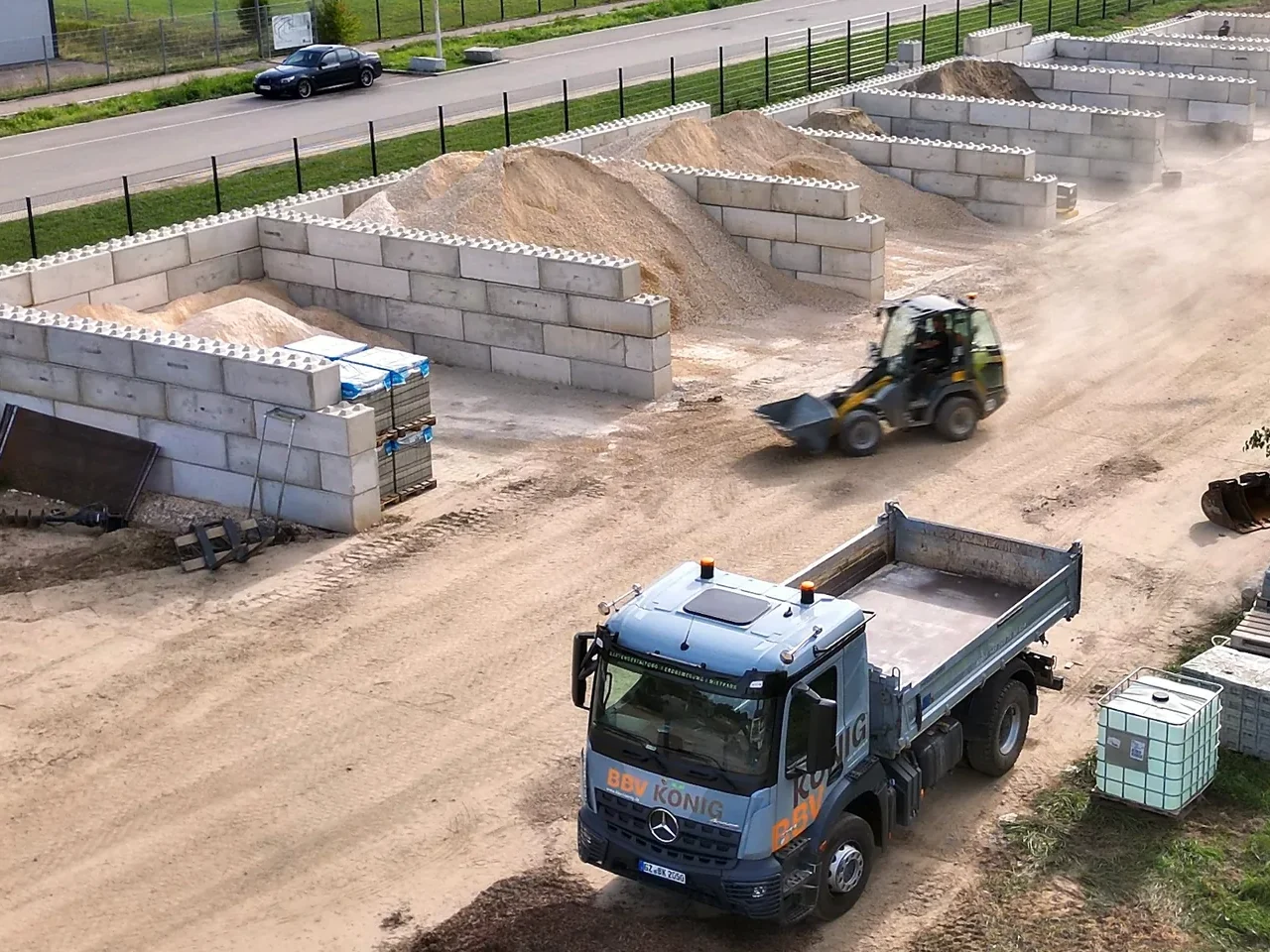 Lagerplatz von BBV König in Leipheim von oben: Boxen aus Betonsteinen mit Sand und Kalkschotter, ein Radlader bei der Arbeit und der Kipper von BBV König im Vordergrund
